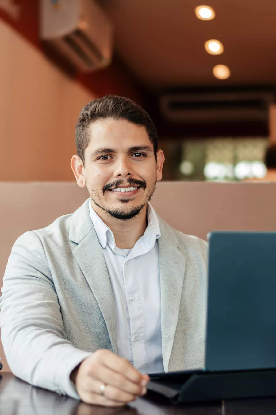 Maurício Filho sorrindo, de blazer claro, trabalhando em um notebook